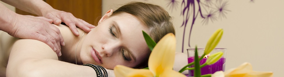 Zrelaksowana młoda kobieta podczas masażu pleców - przed nią kwiaty i świece